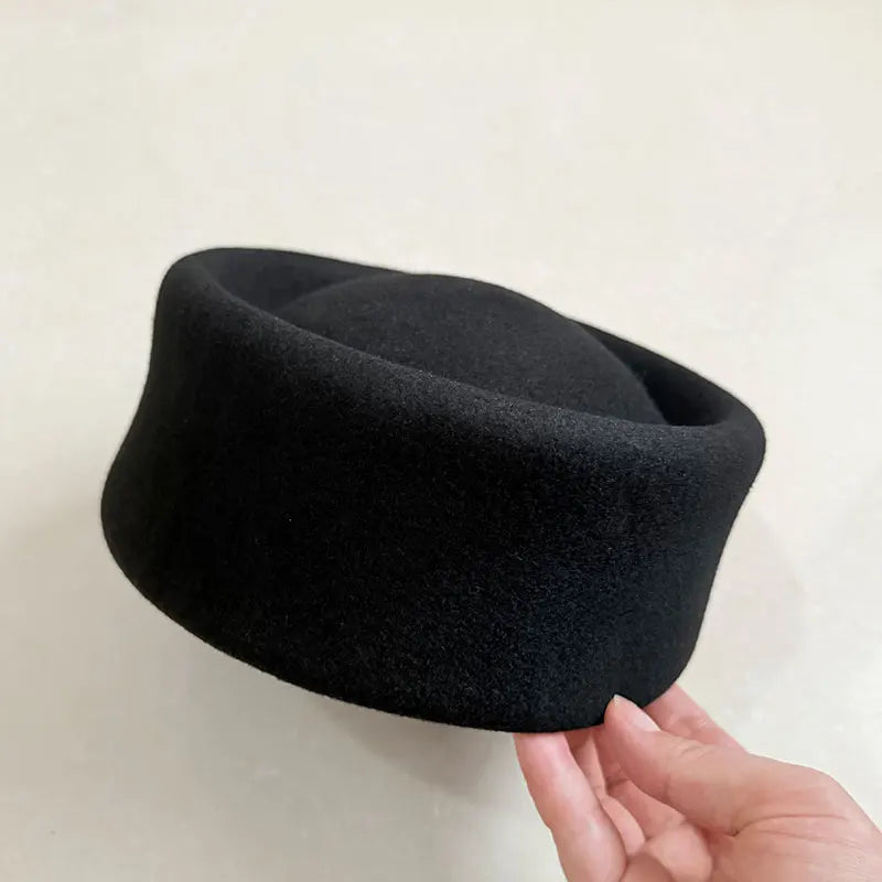 Black fez hat held by a hand against a light background