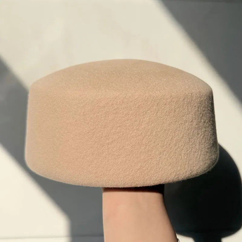 Beige textured hat held by a hand against a neutral background