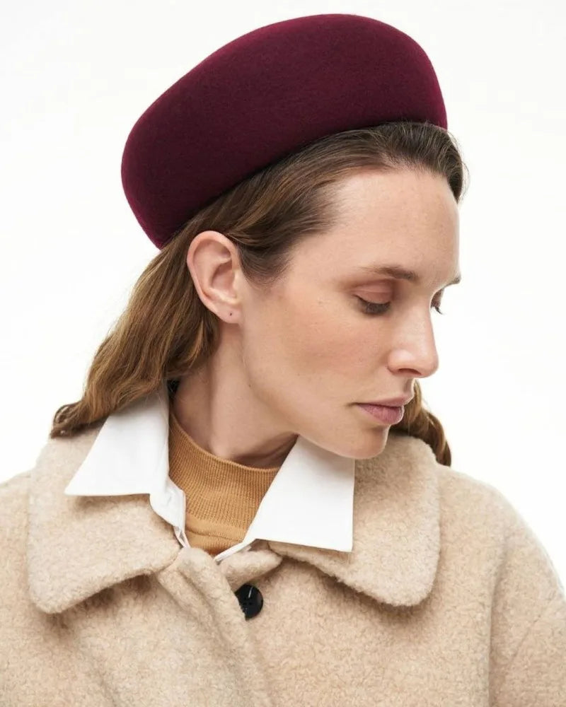 Woman wearing a burgundy beret and beige coat on a white background