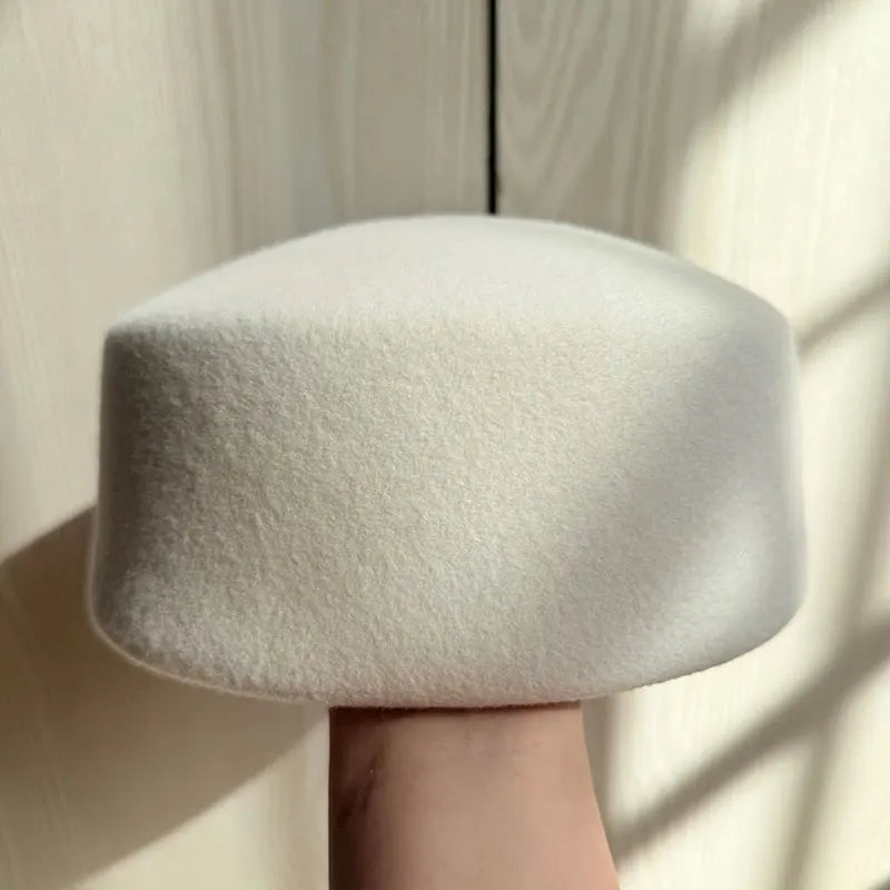 White textured hat held by a hand against a neutral background