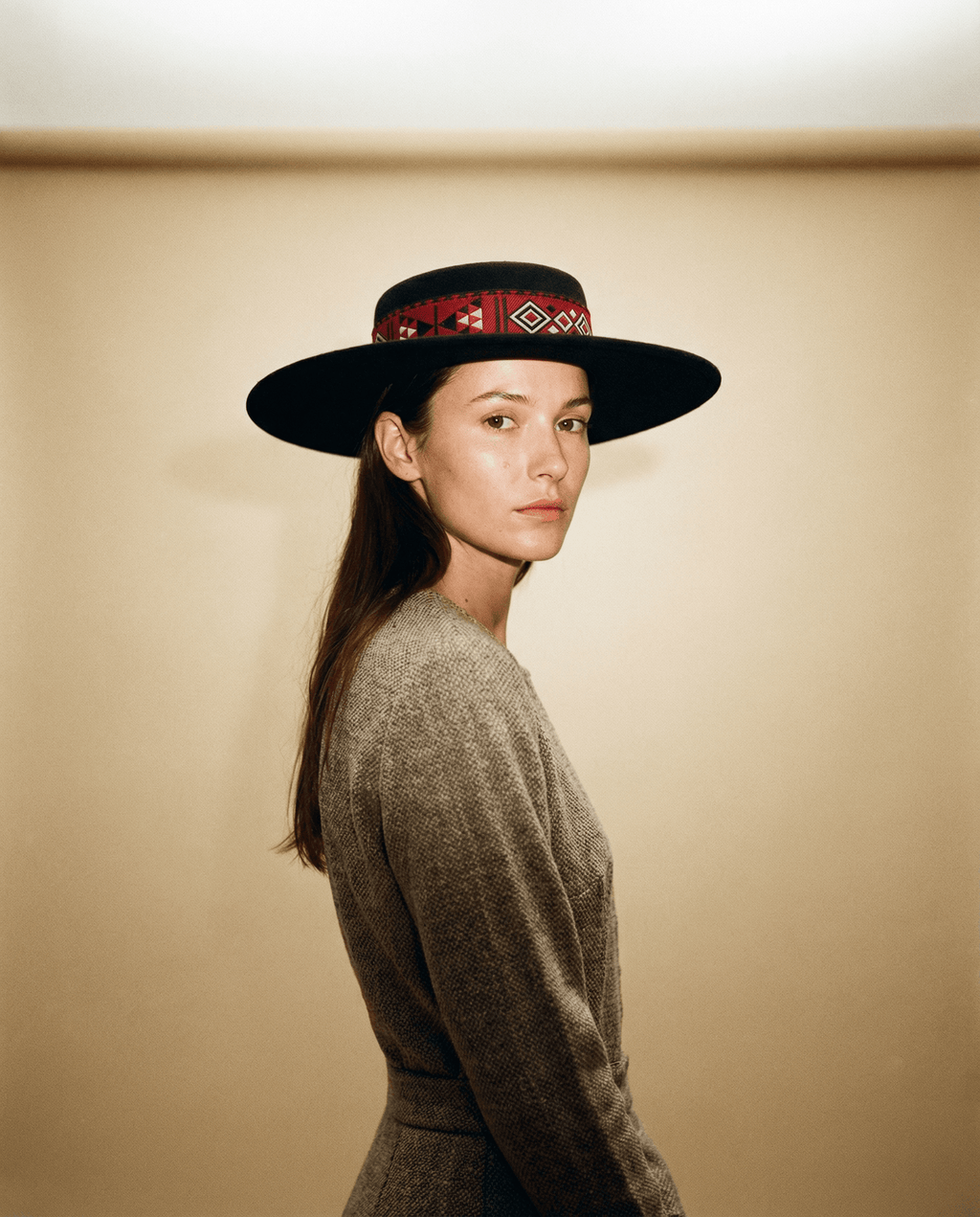 Woman wearing a wide-brimmed hat with a patterned band against a beige background