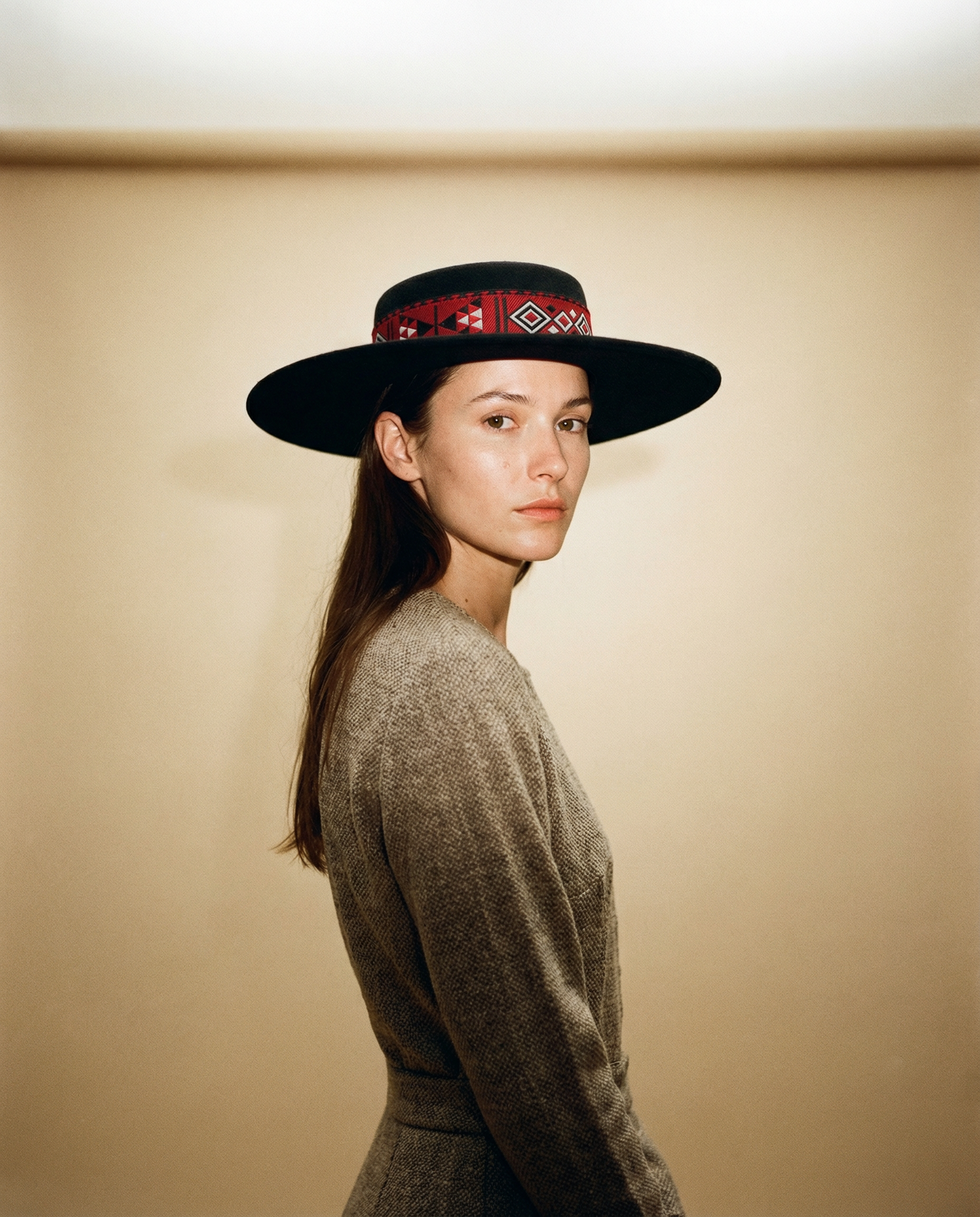 Woman wearing a wide-brimmed hat with a patterned band against a beige background