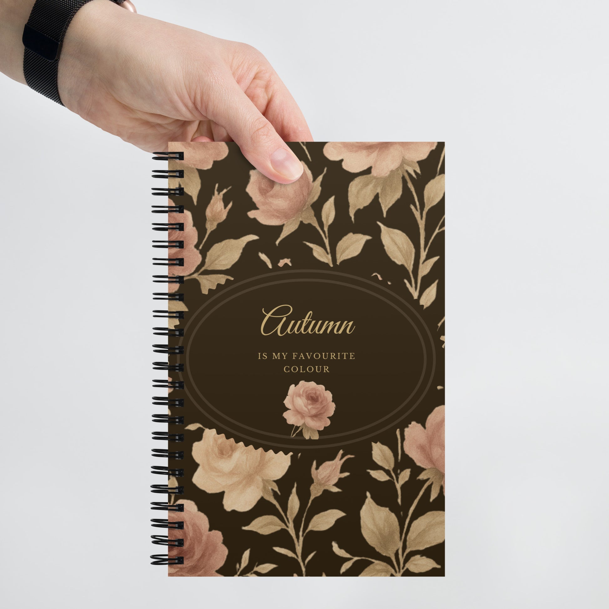 Notebook with floral design and 'Autumn is my favourite colour' text held by a hand on a light gray background